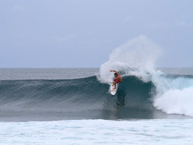 man in a red bathing suit riding a wave during a Bali surf and yoga retreat
