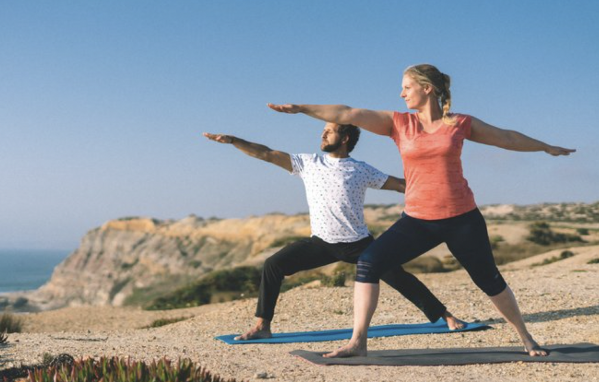 two people practicing yoga on the beach while looking out toward the ocean in Santa Cruz, Portugal