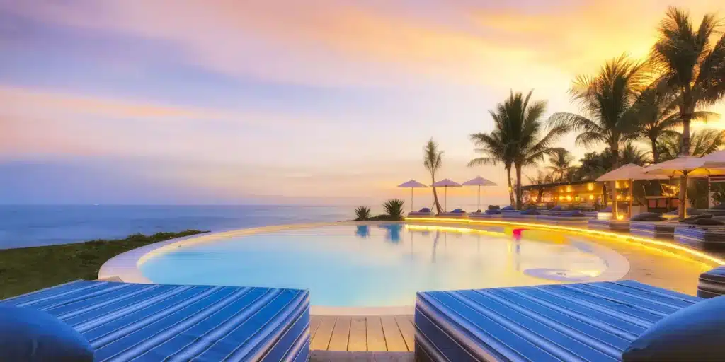 infinity pool surrounded by day beds and palm trees at the  Hotel Komune & Beach Club in Gianyar, Bali